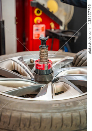 Car wheel positioned on a tire changing machine before removing the tire from the rim. Seasonal tire replacement process at an auto service during winter preparation. Car wheel positioned on a tire changing machine before removing the tire from the rim. Seasonal tire replacement process at an auto service during winter preparation. 132257766