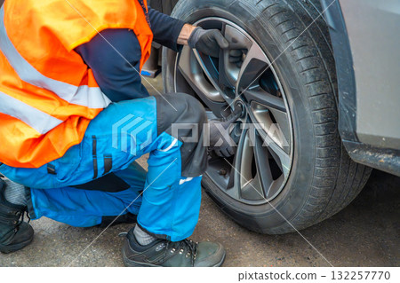Mechanic removing a car wheel during seasonal tire change at an auto service shop. Timely winter tire replacement ensures road safety and compliance with regulations. Mechanic removing a car wheel during seasonal tire change at an auto service shop. Timely winter tire replacement ensures road safety and compliance with regulations. 132257770