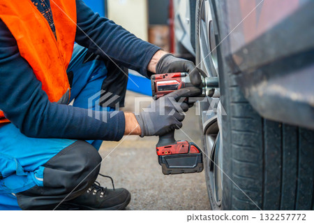 Mechanic using an impact wrench to remove lug nuts from a car wheel. Seasonal tire change and professional car service in preparation for winter. 132257772