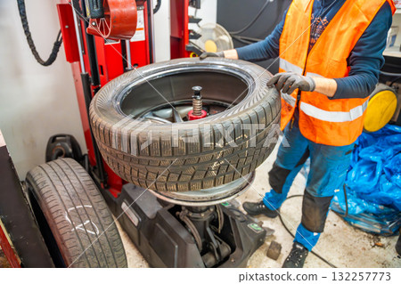 Mechanic replacing a rubber tire on the rim by hand after removal with a tire changing machine. Manual stage of seasonal tire replacement during winter preparation. Mechanic replacing a rubber tire on the rim by hand after removal with a tire changing machine. Manual stage of seasonal tire replacement during winter preparation. 132257773