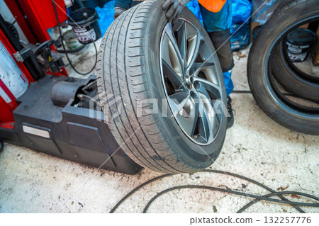 Tire changing machine lifting a car wheel for further separation of tire and rim. Technical stage of seasonal tire replacement at a professional auto service. Tire changing machine lifting a car wheel for further separation of tire and rim. Technical stage of seasonal tire replacement at a professional auto service. 132257776