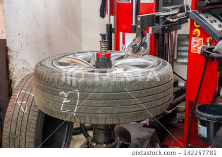 Tire changing machine removing the rubber tire from the rim using a rotating metal arm. Essential step in seasonal wheel replacement at a professional auto workshop. 132257781