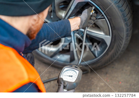 Worker checking tire pressure with gauge after seasonal wheel replacement. Final step of winter tire preparation in auto service in Czech Republic. 132257784