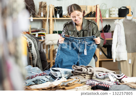 Positive young girl choosing jeans pantaloons in clothing store 132257805