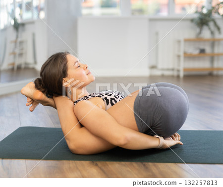 Young sporty attractive woman wearing sportswear practicing yoga, doing Halasana exercise and variety of Plough pose, difficult yoga pose in modern yoga studio 132257813
