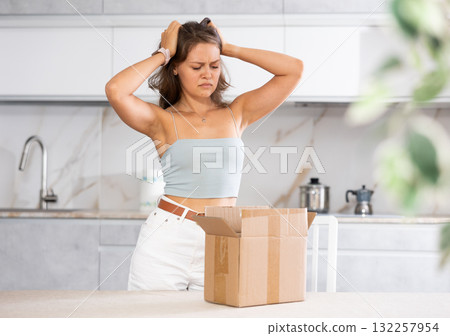 Young upset woman holding open box in kitchen 132257954