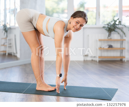 Smiling young woman doing Ardha Uttanasana in studio 132257976