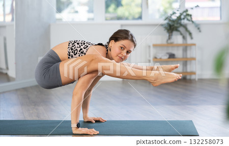 Active young girl yogi doing firefly yoga pose in gym. Woman practicing advanced yoga 132258073