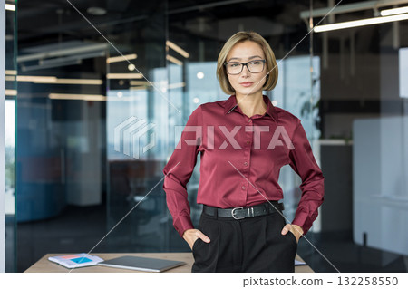 Professional young businesswoman standing in a contemporary office setting, showing confidence, leadership, determination, and success while looking directly forward Professional young businesswoman standing in a contemporary office setting, showing confidence, leadership, determination, and success while looking directly forward 132258550