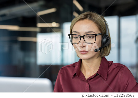 Woman wearing a professional headset with a microphone, focusing on her work, representing concepts of customer support, call center operations, and remote communications in a modern office setting Woman wearing a professional headset with a microphone, focusing on her work, representing concepts of customer support, call center operations, and remote communications in a modern office setting 132258562