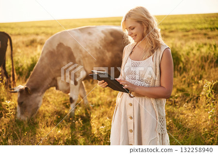 Digital tablet in hands and cows that are behind. Young woman is on the farm 132258940