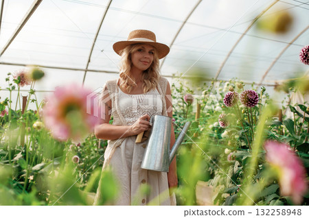 Watering can in hands. Beautiful woman is in the greenhouse Watering can in hands. Beautiful woman is in the greenhouse 132258948