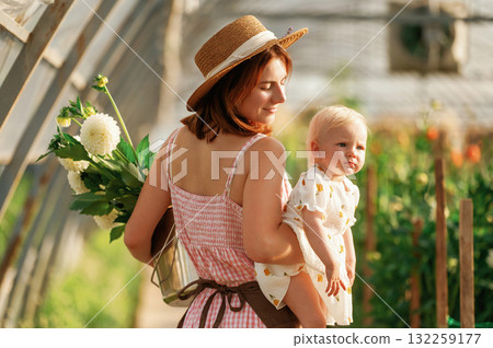 Rear view, holding baby in hand. Mother and daughter are in the greenhouse Rear view, holding baby in hand. Mother and daughter are in the greenhouse 132259177