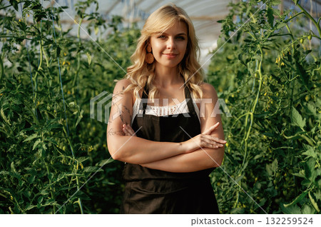 Standing with arms crossed. Beautiful woman is in the greenhouse Standing with arms crossed. Beautiful woman is in the greenhouse 132259524