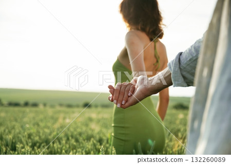 Woman is leading the man by a hand. Lovely couple are on the agricultural field together 132260089