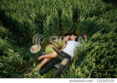 Couple is lying down on the agricultural field with high wheat that is growing Couple is lying down on the agricultural field with high wheat that is growing 132260108