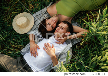 Couple is lying down on the agricultural field with high wheat that is growing Couple is lying down on the agricultural field with high wheat that is growing 132260111