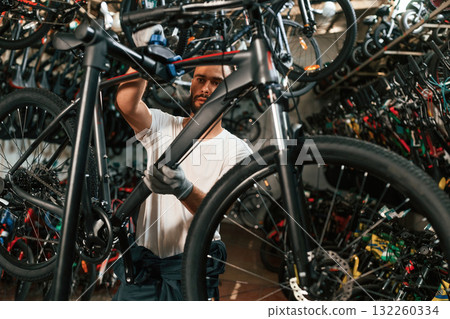 In grey colored gloves. Repair man in bicycle shop, working in store In grey colored gloves. Repair man in bicycle shop, working in store 132260334