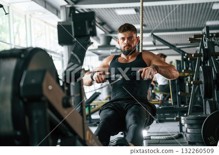 Sitting, doing stamina exercise. Strong muscular man is working out in the gym 132260509