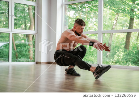Daytime, trees outside the windows. Strong muscular man is working out in the gym 132260559