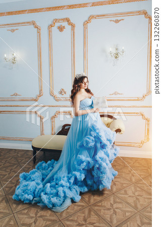 pregnant girl sitting on the floor in a lush blue dress. girl with dark hair wearing a crown.pregnant girl holding a gift. High quality photo 132260870