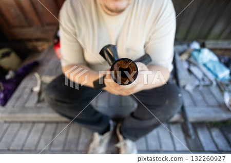 Man demonstrating a section of an old water pipe revealing extreme rust and mineral buildup, indicating severe corrosion and a major blockage impacting water flow and plumbing system efficiency. 132260927