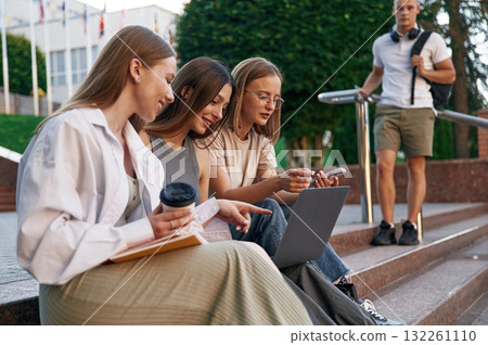 Relaxed, on the stairs, with laptop. Group of students are outside together 132261110