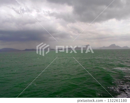Boat Deck View of a Vast Ocean Horizon with Distant Land Under a Cloudy Sky 132261180