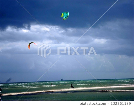 Kitesurfers Soaring Over Coastal Waters Under a Cloudy Sky on a Windy Day 132261189