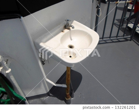 A White Sink on the Deck of a Boat with Railing and Pipes in the Background A White Sink on the Deck of a Boat with Railing and Pipes in the Background 132261201