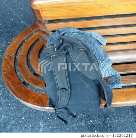 A Wooden Bench at a Train Station with a Blue Backpack and Denim Jacket on It 132261217