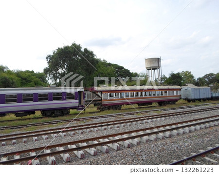 Train Yard with Purple and Red Trains Near a Water Tower Under a Cloudy Sky 132261223