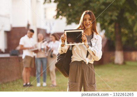 Woman is showing digital tablet, copy space. Group of students are outside together 132261265