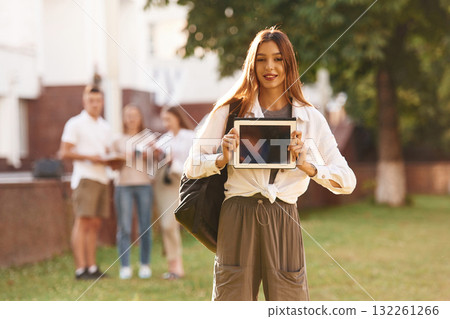Woman is showing digital tablet, copy space. Group of students are outside together 132261266