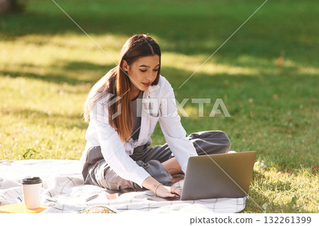 Silver colored laptop, sitting. Beautiful female student is outdoors near the university Silver colored laptop, sitting. Beautiful female student is outdoors near the university 132261399