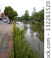 Riverside Pathway with Yellow Flowers and Lush Greenery Along a Quiet Waterway 132261520