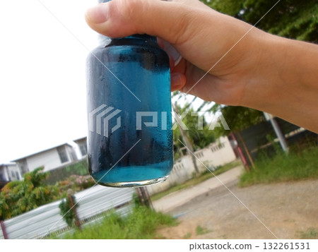 A Hand Grasping a Vibrant Blue Glass Bottle in an Outdoor Garden Setting with Blurred Background 132261531