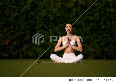 Doing yoga exercises. Attractive young fitness woman is on the green grass at daytime Doing yoga exercises. Attractive young fitness woman is on the green grass at daytime 132261569