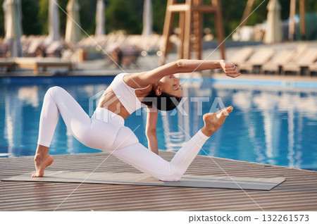 Focused on flexible exercises. Fitness woman is near the pool Focused on flexible exercises. Fitness woman is near the pool 132261573