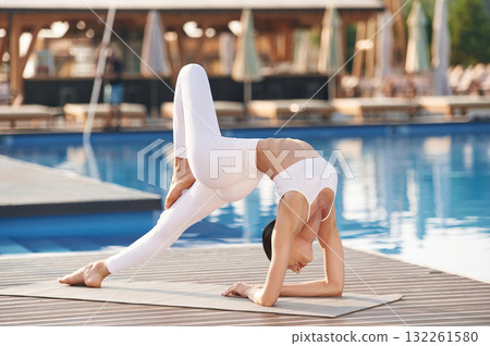 Focused on flexible exercises. Fitness woman is near the pool Focused on flexible exercises. Fitness woman is near the pool 132261580