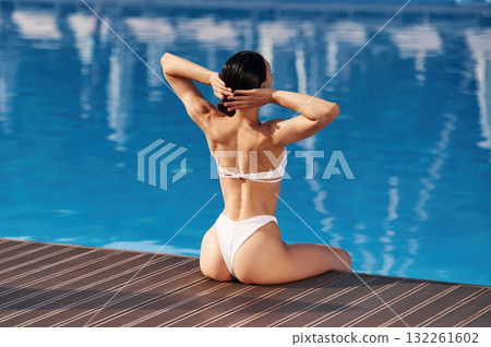 Back view, sitting. Beautiful woman in bikini is resting by the pool 132261602