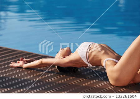 Lying down, close up view. Beautiful woman in bikini is resting by the pool Lying down, close up view. Beautiful woman in bikini is resting by the pool 132261604