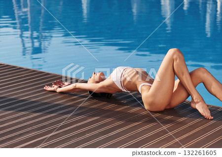 Lying down, close up view. Beautiful woman in bikini is resting by the pool Lying down, close up view. Beautiful woman in bikini is resting by the pool 132261605