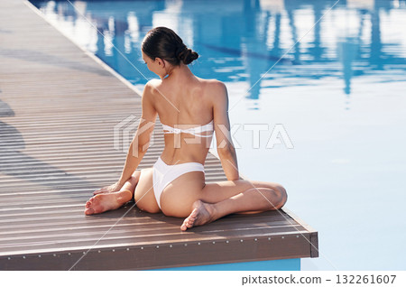 Back view, sitting. Beautiful woman in bikini is resting by the pool 132261607