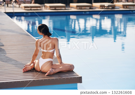 Back view, sitting. Beautiful woman in bikini is resting by the pool 132261608