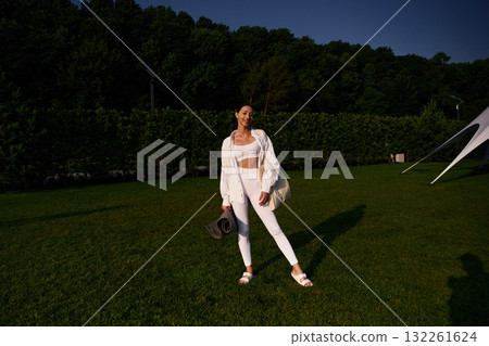 Happy smiling woman is standing on the green grass, trees at background Happy smiling woman is standing on the green grass, trees at background 132261624