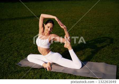 On the yoga mat, exercises. Attractive young fitness woman is on the green grass at daytime 132261649