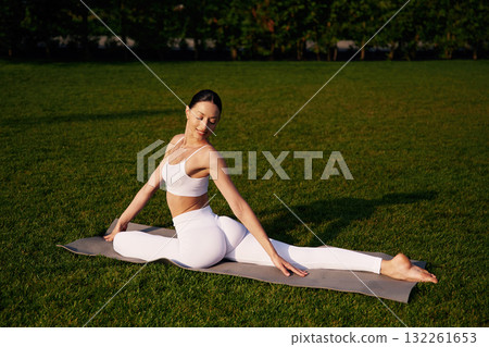 On the yoga mat, exercises. Attractive young fitness woman is on the green grass at daytime On the yoga mat, exercises. Attractive young fitness woman is on the green grass at daytime 132261653