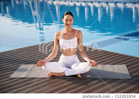 Brown ground, sitting, smiling. Fitness woman is near the pool Brown ground, sitting, smiling. Fitness woman is near the pool 132261654