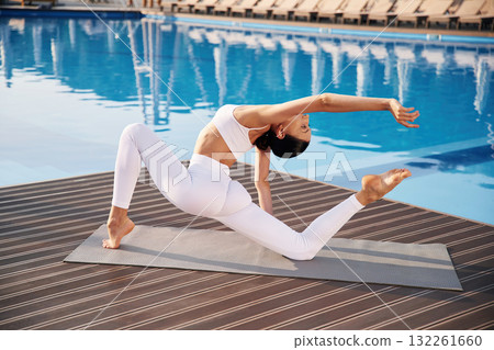 Busy by doing yoga exercise. Fitness woman is near the pool Busy by doing yoga exercise. Fitness woman is near the pool 132261660